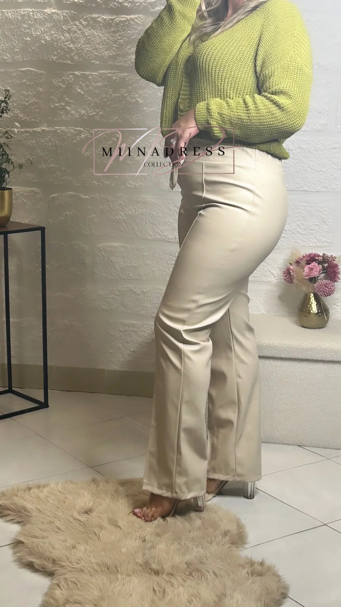 Femme portant un pull vert en maille et un pantalon beige, chaussures à talon transparent, intérieur élégant