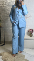 Femme portant un tailleur pantalon bleu clair tendance, ambiance chic et moderne intérieur.