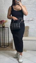 Femme en robe noire longue ajustée, sac à main matelassé noir, baskets blanches tendance.