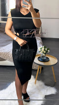 Femme en robe noire chic, sac matelassé, posant dans une chambre moderne, style élégant.