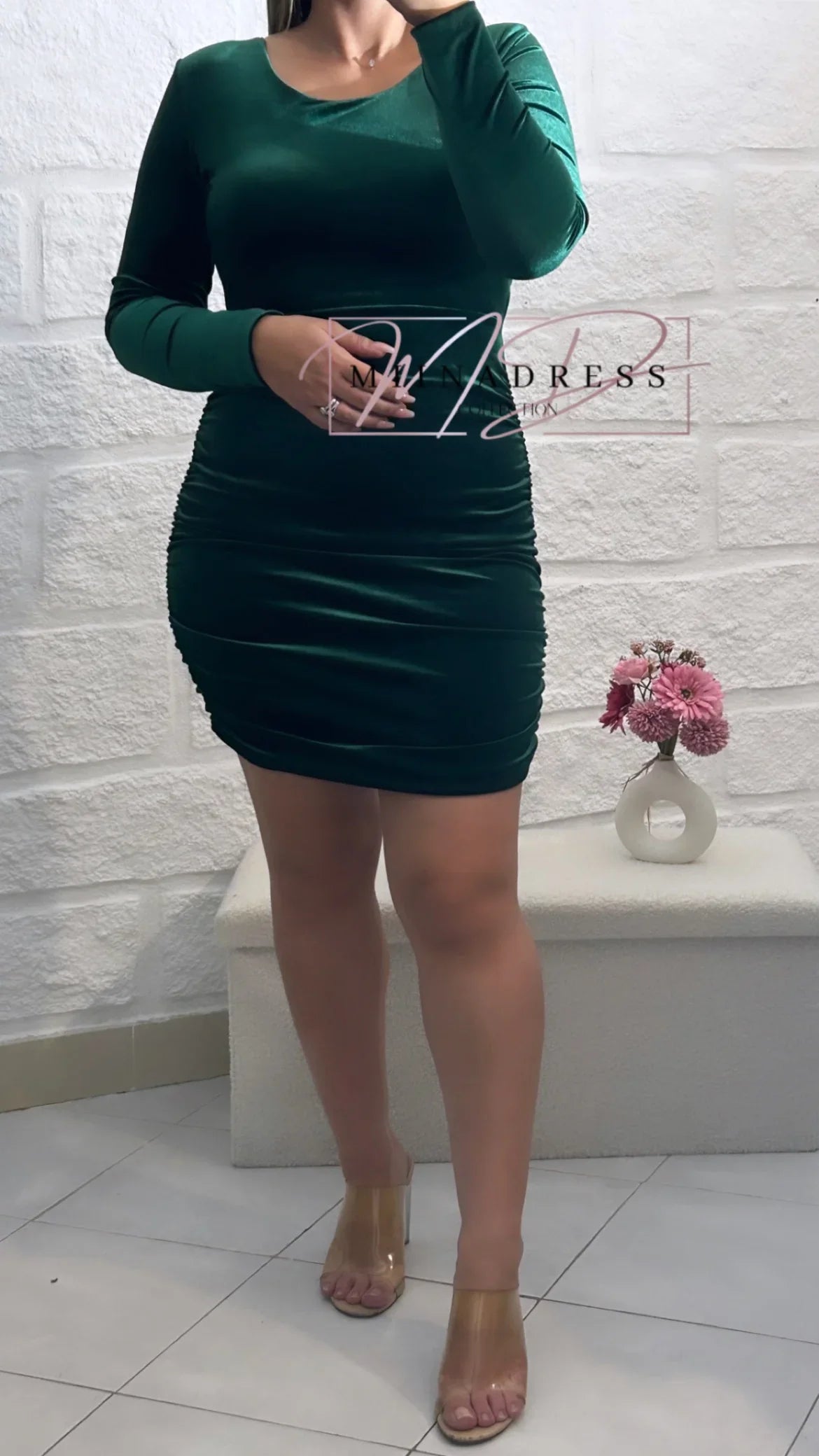 Robe moulante vert foncé à manches longues, femme debout, déco fleurs, ambiance chic