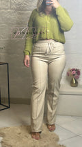 Femme portant un gilet vert en maille et un pantalon beige taille haute, look moderne et chic.