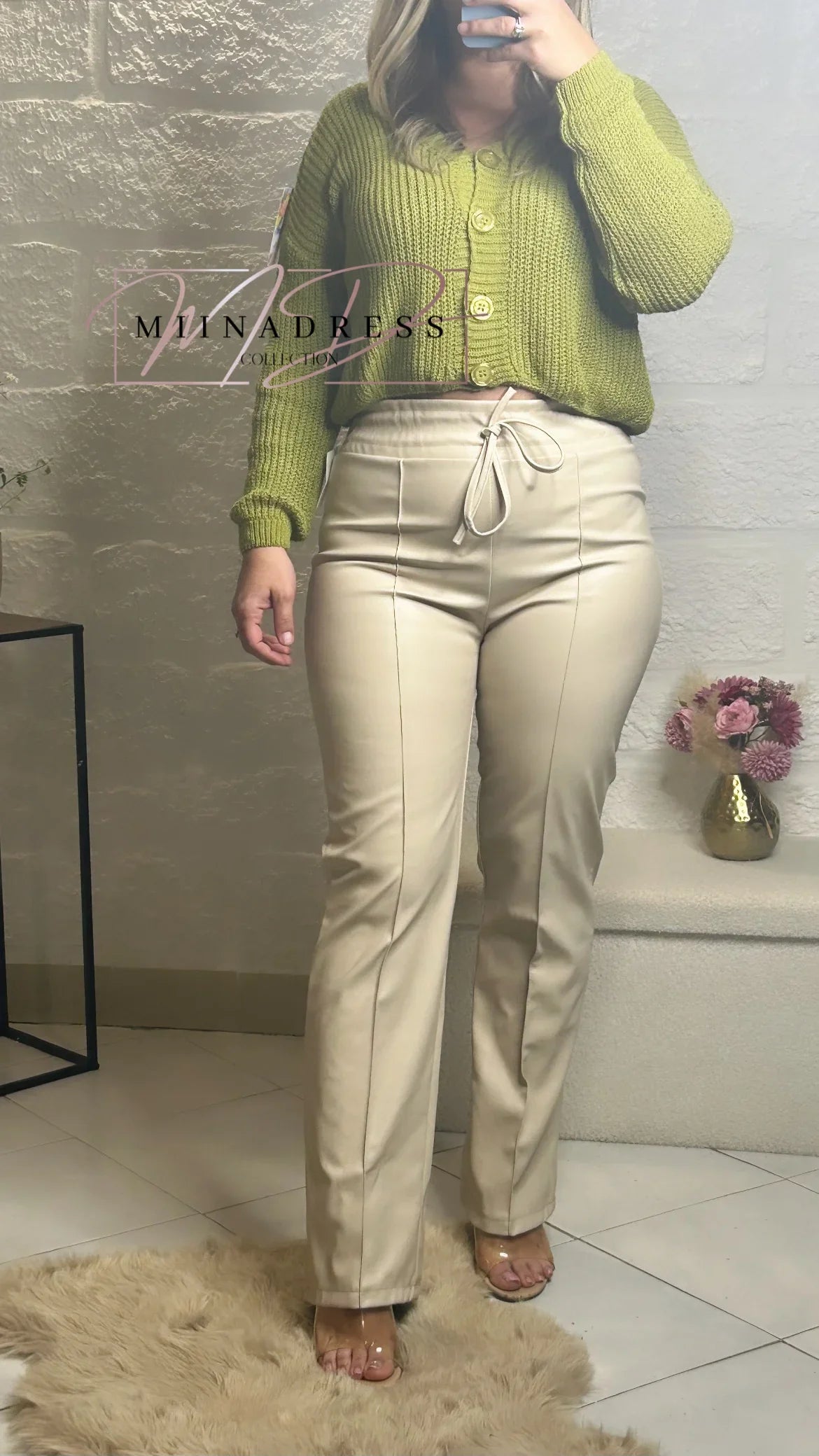 Femme portant un gilet vert en maille et un pantalon beige taille haute, look moderne et chic.