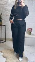 Femme portant un pull noir ajouré et pantalon large noir, look chic décontracté