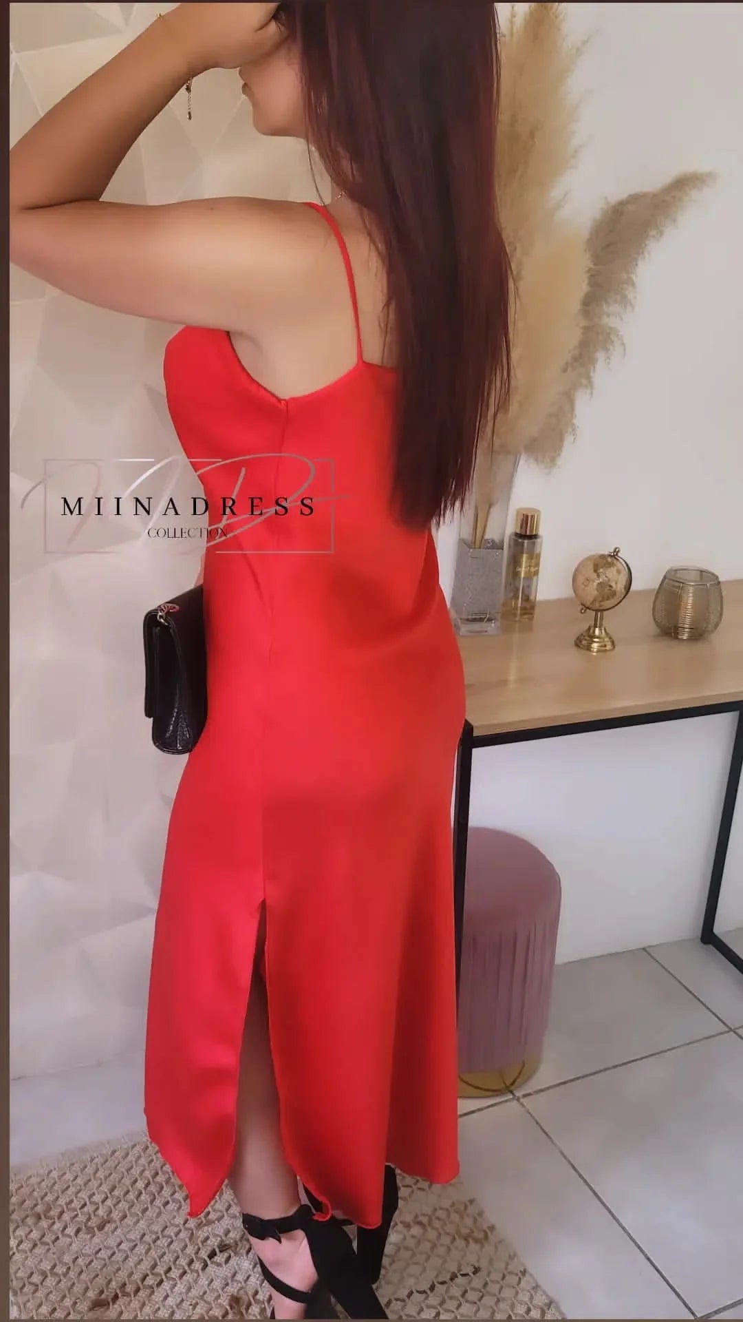Femme en robe rouge satinée fendue, debout près d'une coiffeuse moderne, look chic