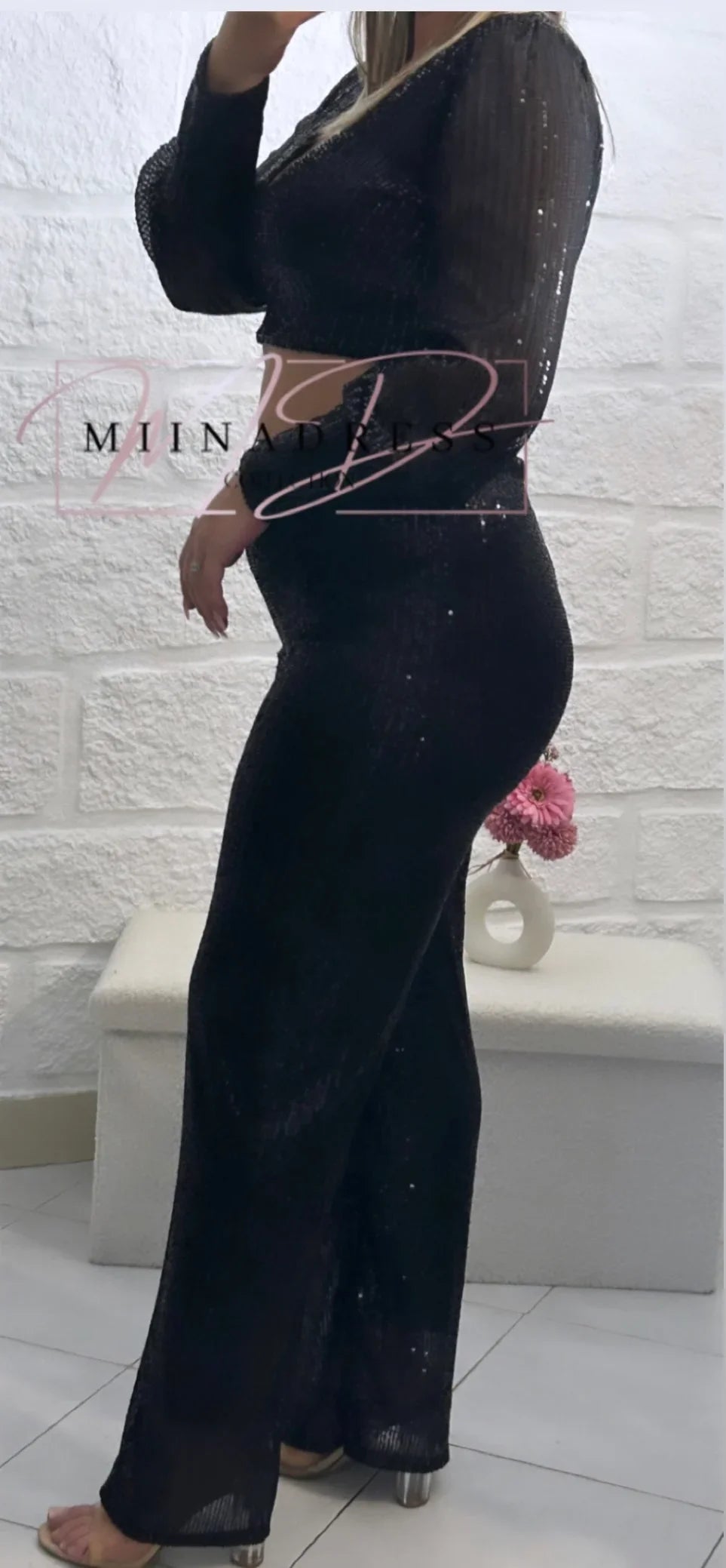 Femme portant un ensemble noir brillant, haut manches longues et pantalon large, style chic