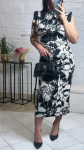 Femme portant une robe midi noire et blanche à motifs abstraits, sac noir élégant et escarpins