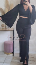 Femme portant un ensemble noir élégant avec haut à manches larges et pantalon taille haute.