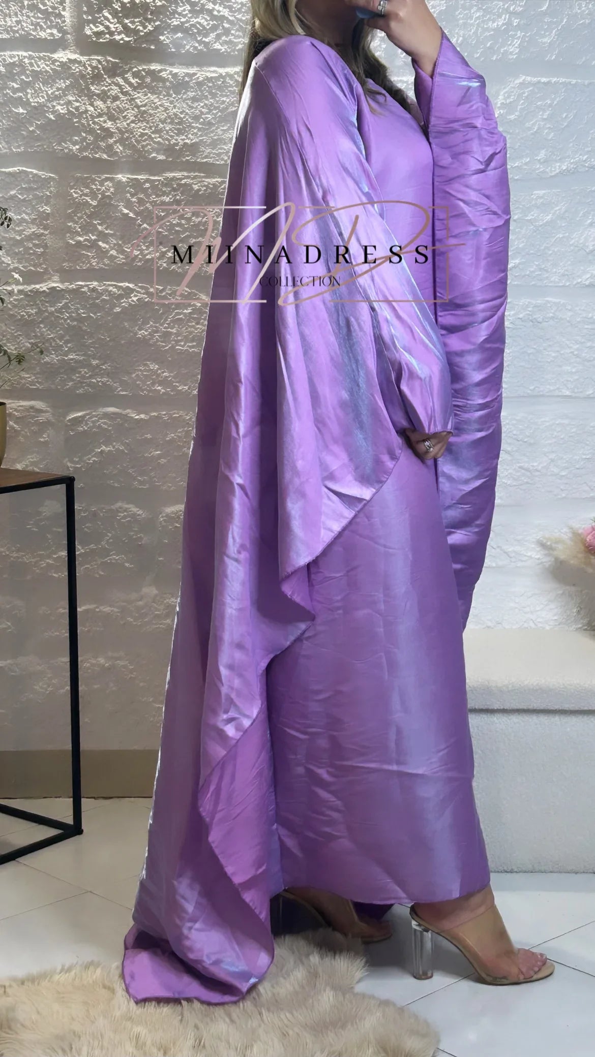 Femme portant une abaya longue en satin violet, manches amples, talons transparents.