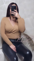 Femme en pull camel col croisé et pantalon simili cuir noir, look chic décontracté.