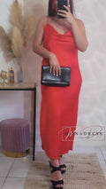 Femme portant une robe longue rouge à bretelles, escarpins noirs, pochette noire élégante.